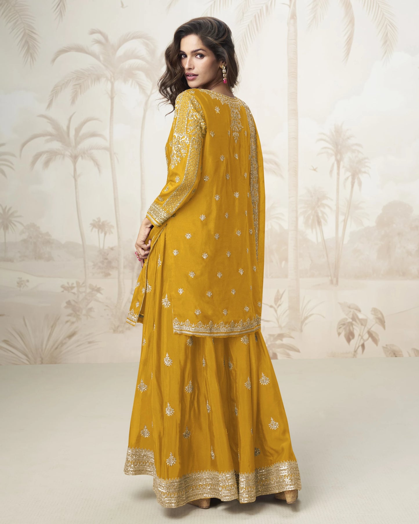 Woman wearing a mustard yellow traditional outfit with intricate patterns against a neutral background