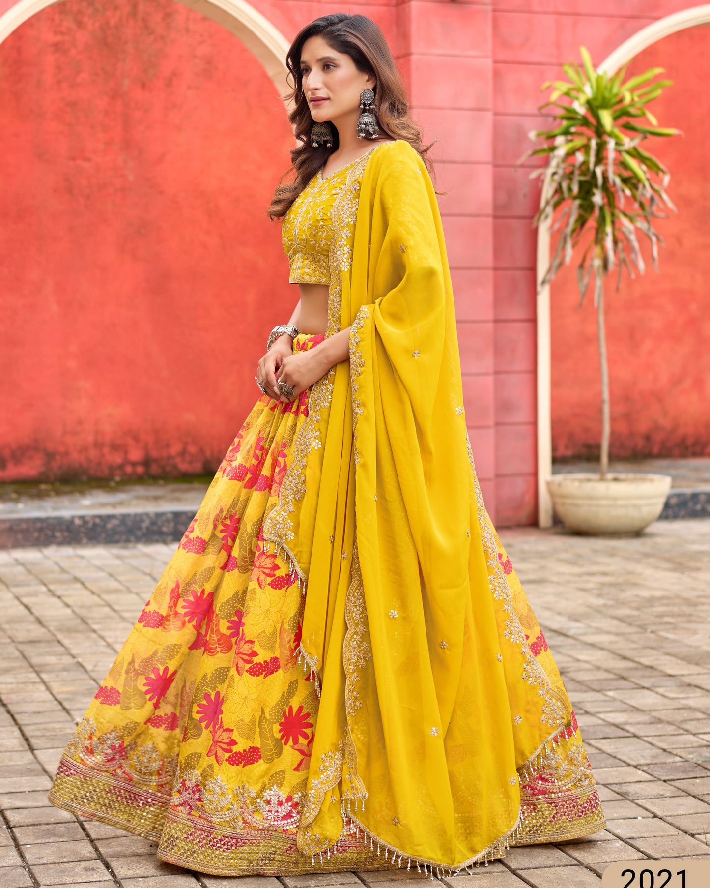 Woman wearing a yellow saree with floral patterns against a red wall.