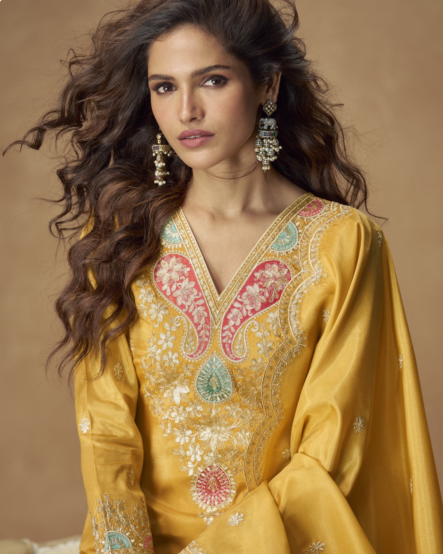 Woman wearing a yellow embroidered traditional outfit with a brown background