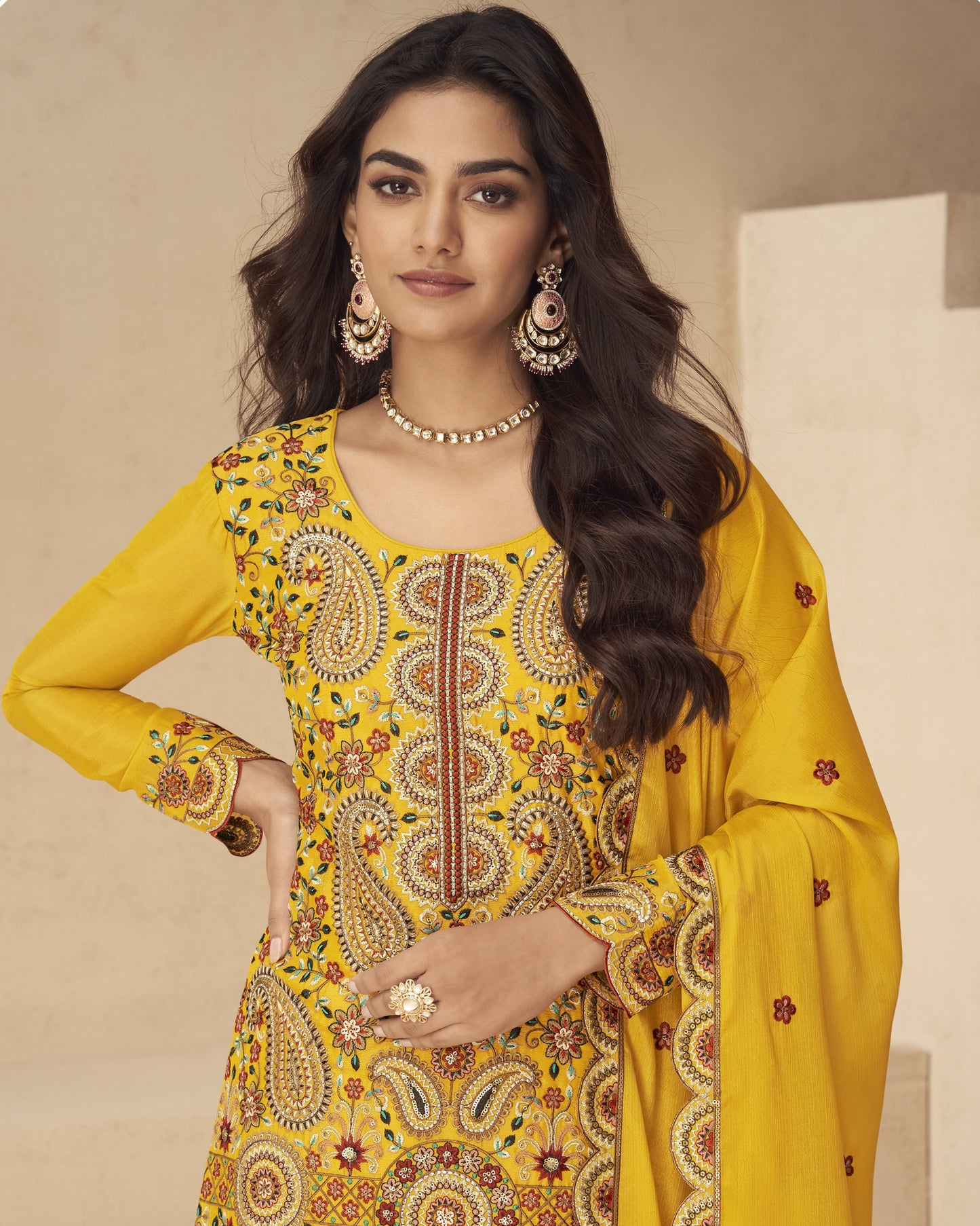 Woman wearing a yellow embroidered traditional outfit with jewelry against a neutral background