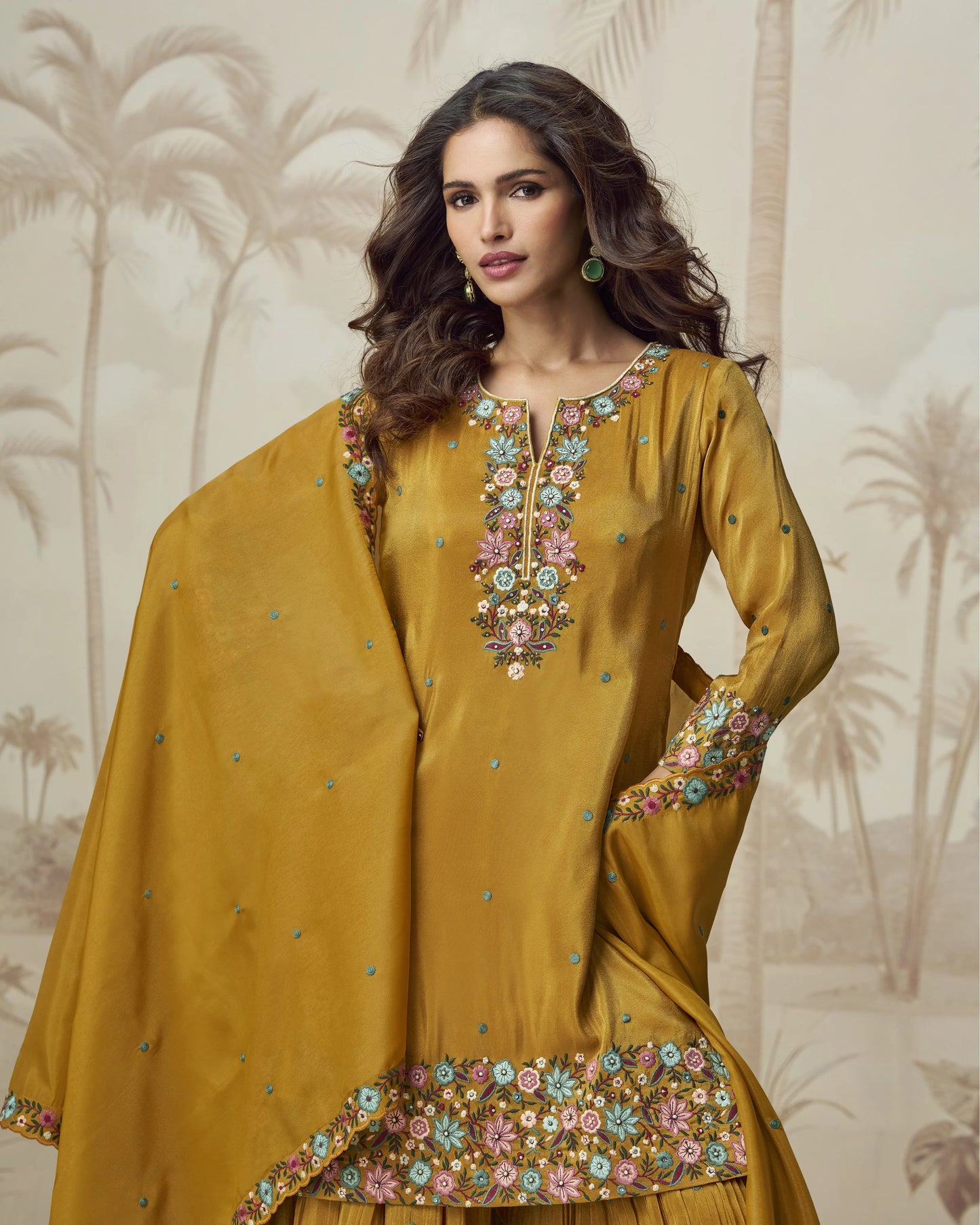 Woman wearing a mustard yellow traditional outfit with floral embroidery against a neutral background