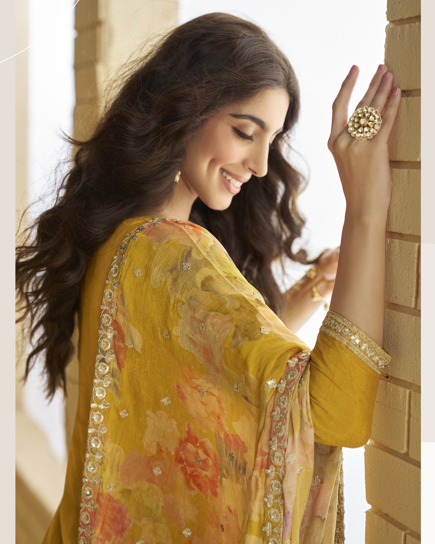 Woman wearing a yellow saree with floral patterns, standing against a light background.