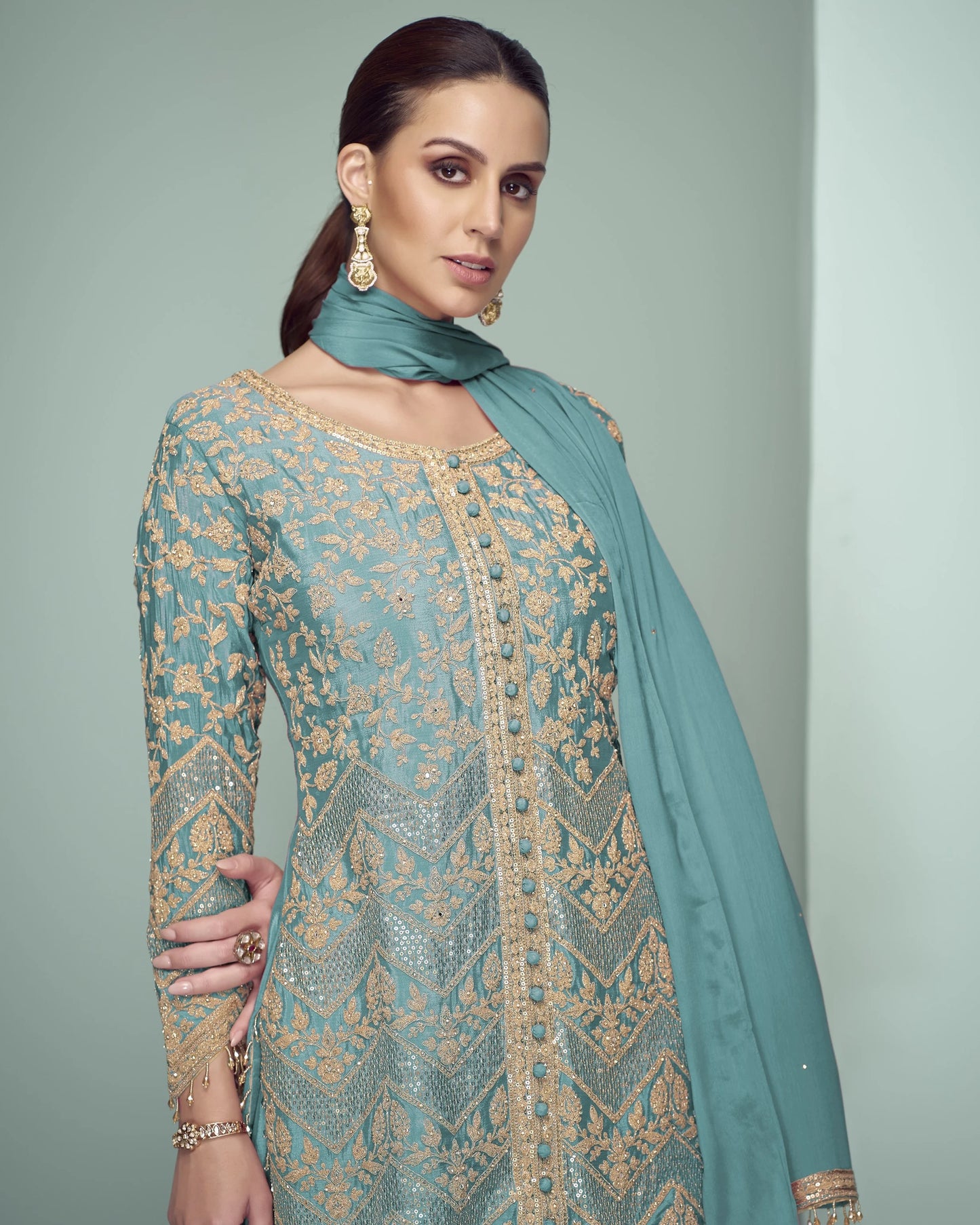 Woman wearing a traditional embroidered outfit with a matching dupatta against a plain background