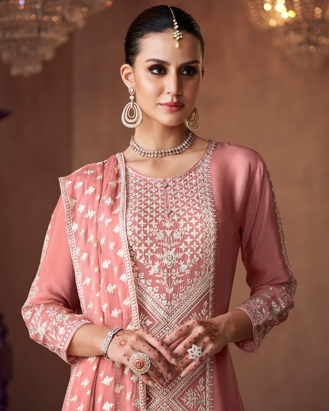 Woman wearing a pink embroidered traditional outfit with jewelry against a warm-toned background