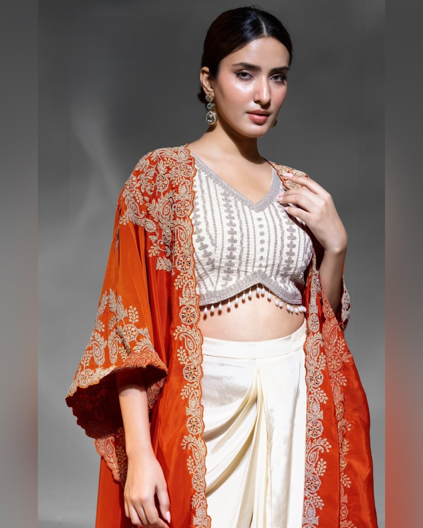 Woman wearing a traditional outfit with a white blouse, orange dupatta, and white saree.