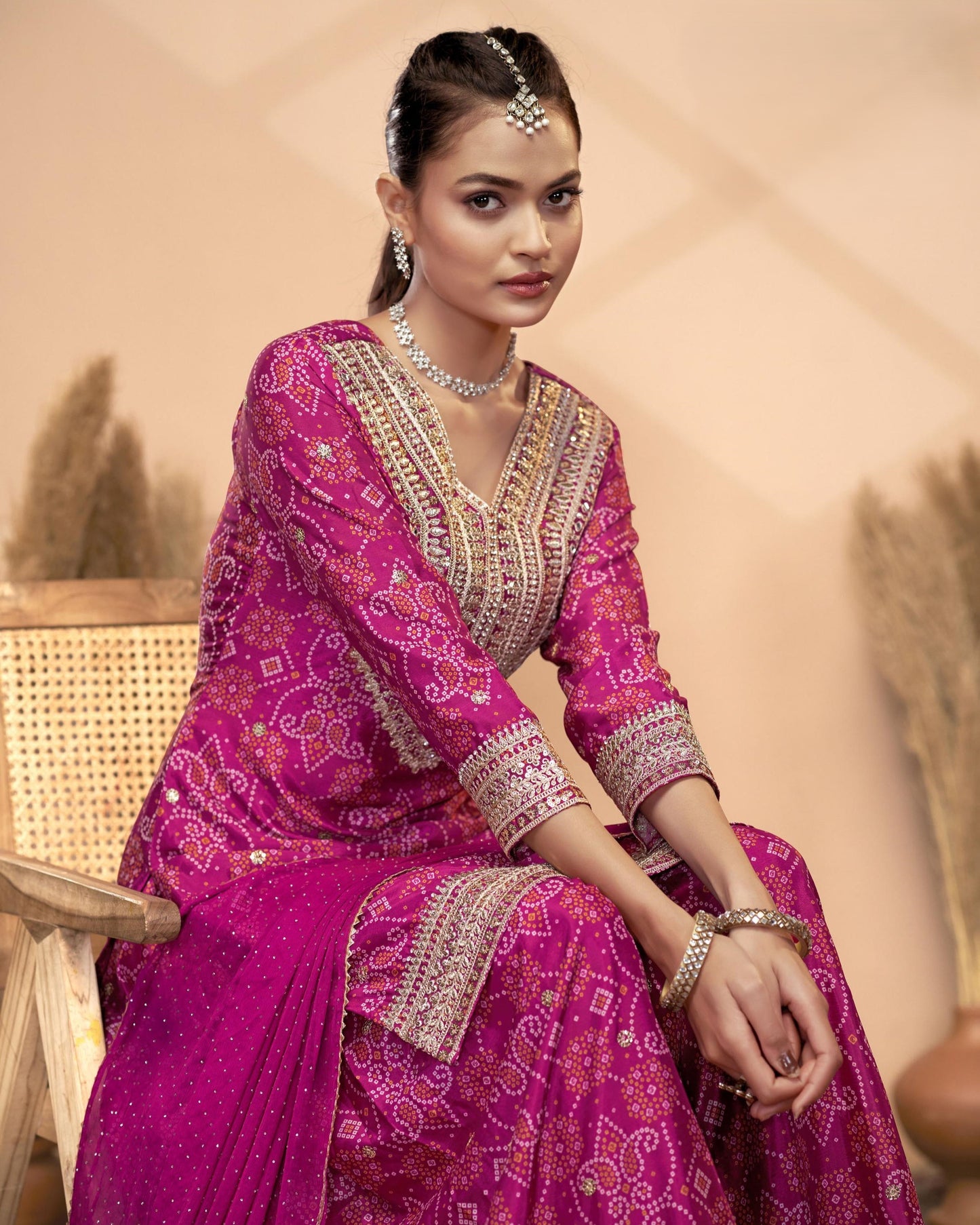 Woman in a vibrant pink traditional outfit with intricate patterns, sitting outdoors.