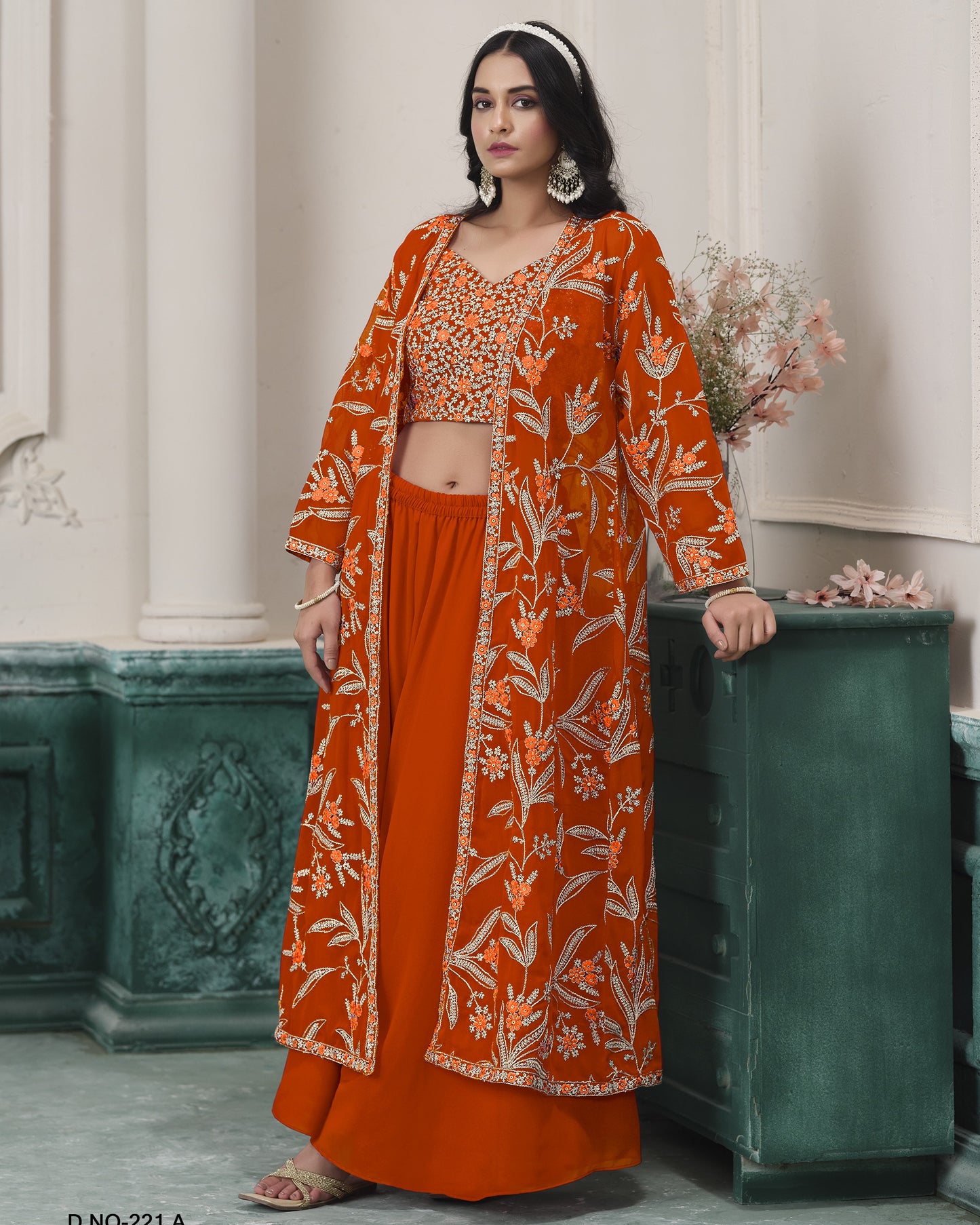 Woman wearing an orange floral outfit standing against a decorative wall.