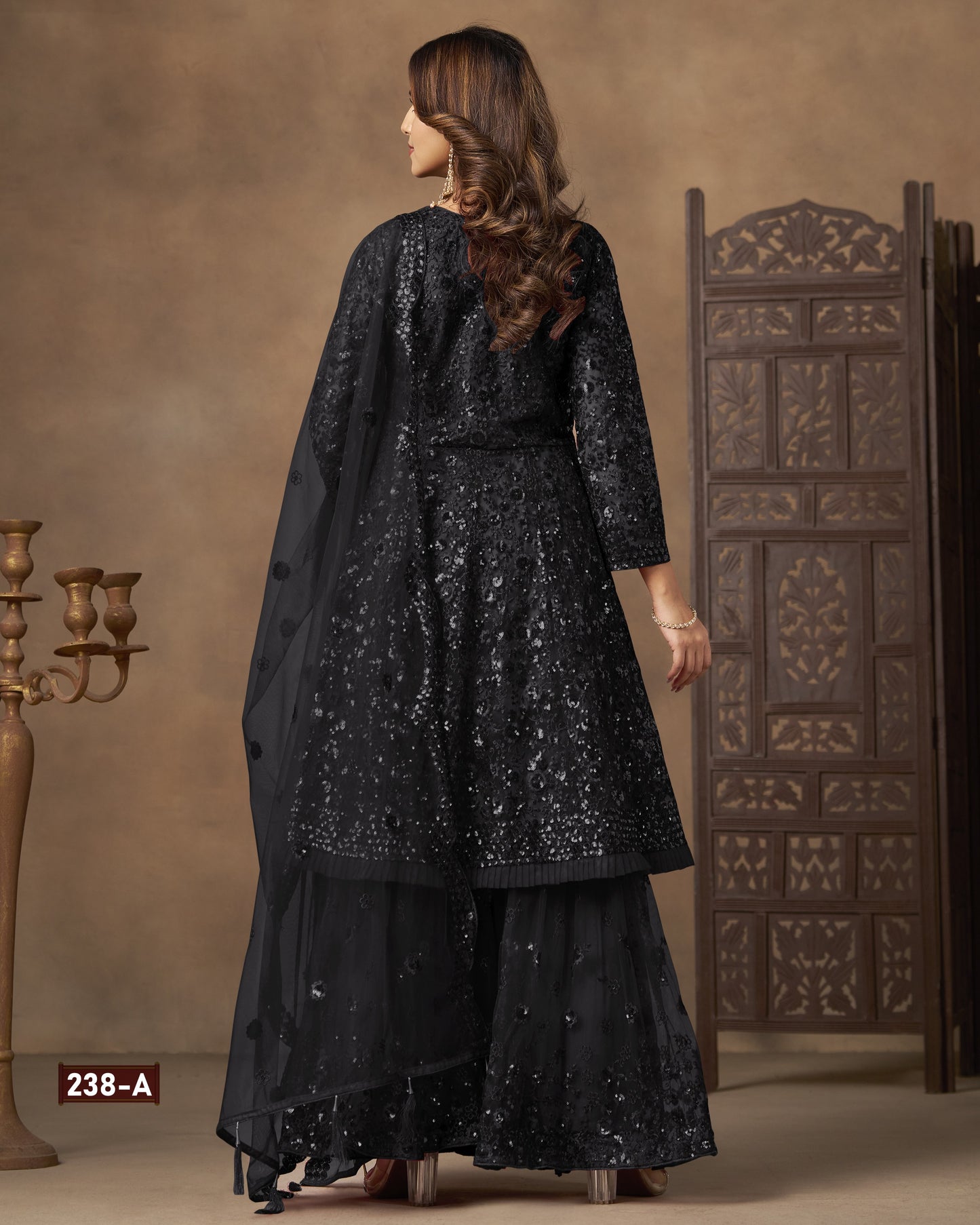 Woman wearing a black embroidered outfit in a decorated room.