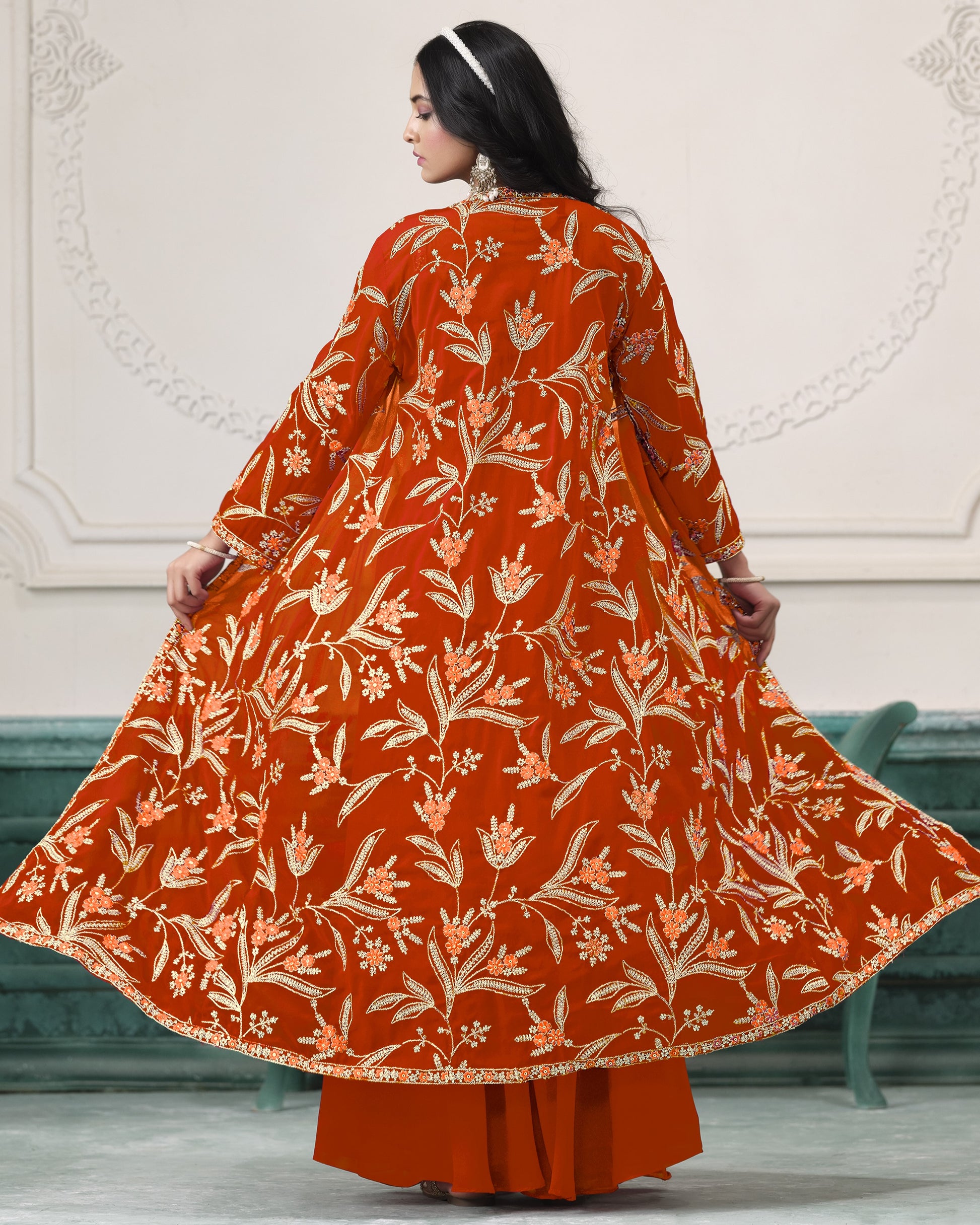 Woman wearing a rust-colored floral patterned outfit against a white wall.