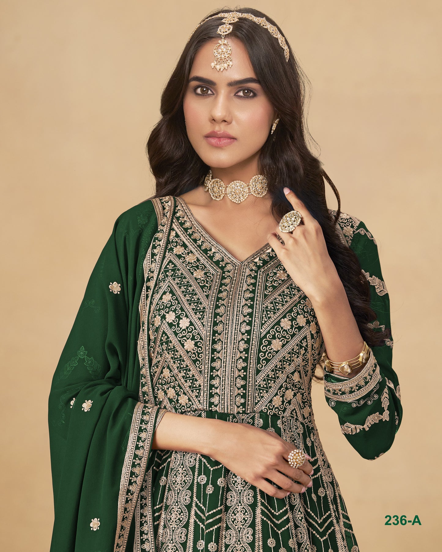 Woman wearing a green and gold traditional outfit with jewelry on a beige background