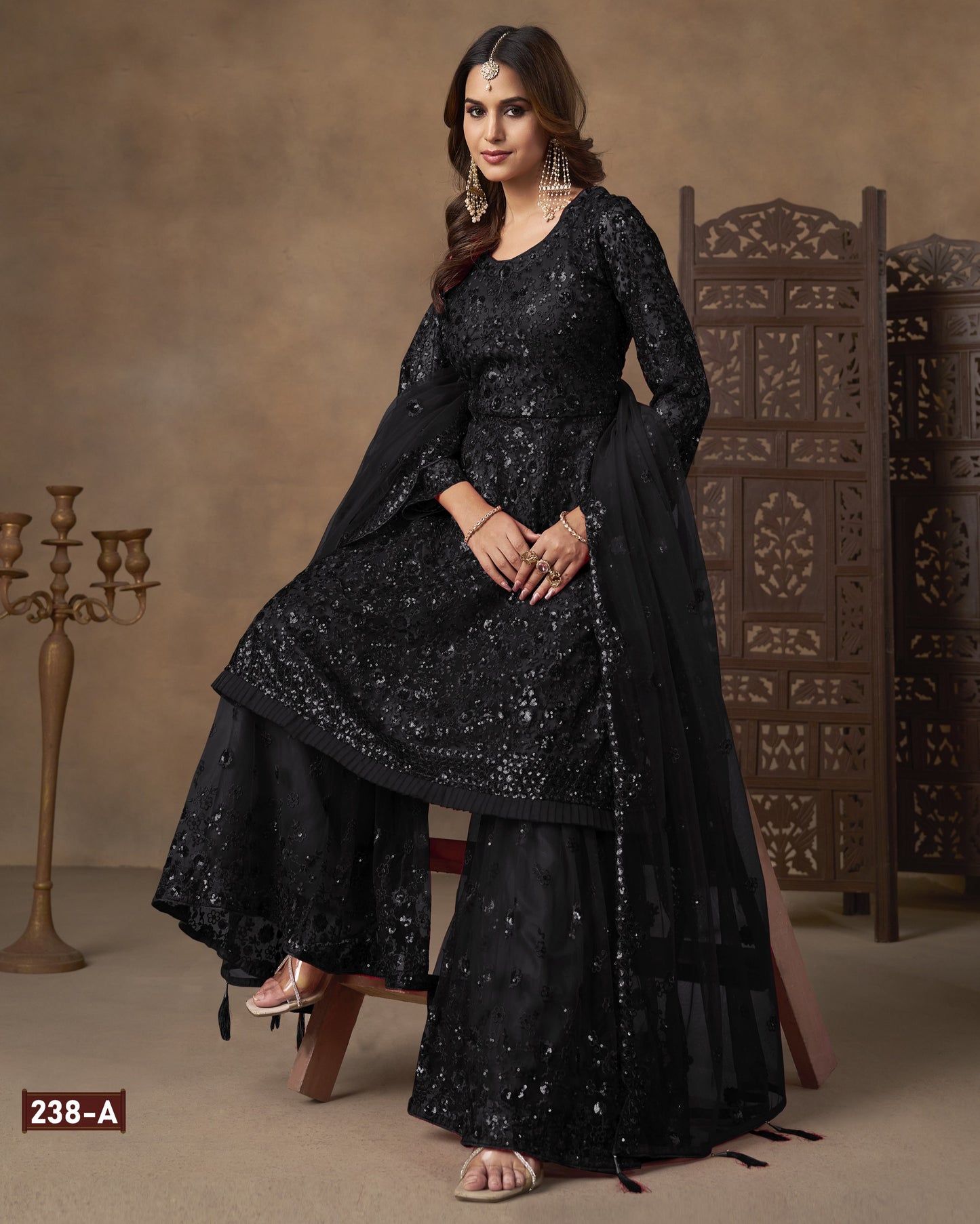 Woman wearing a black traditional outfit with intricate designs in a decorated room.