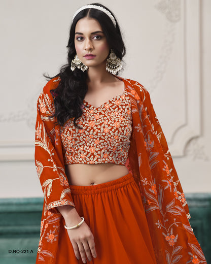 Woman wearing an orange traditional outfit with floral patterns against a decorative wall.