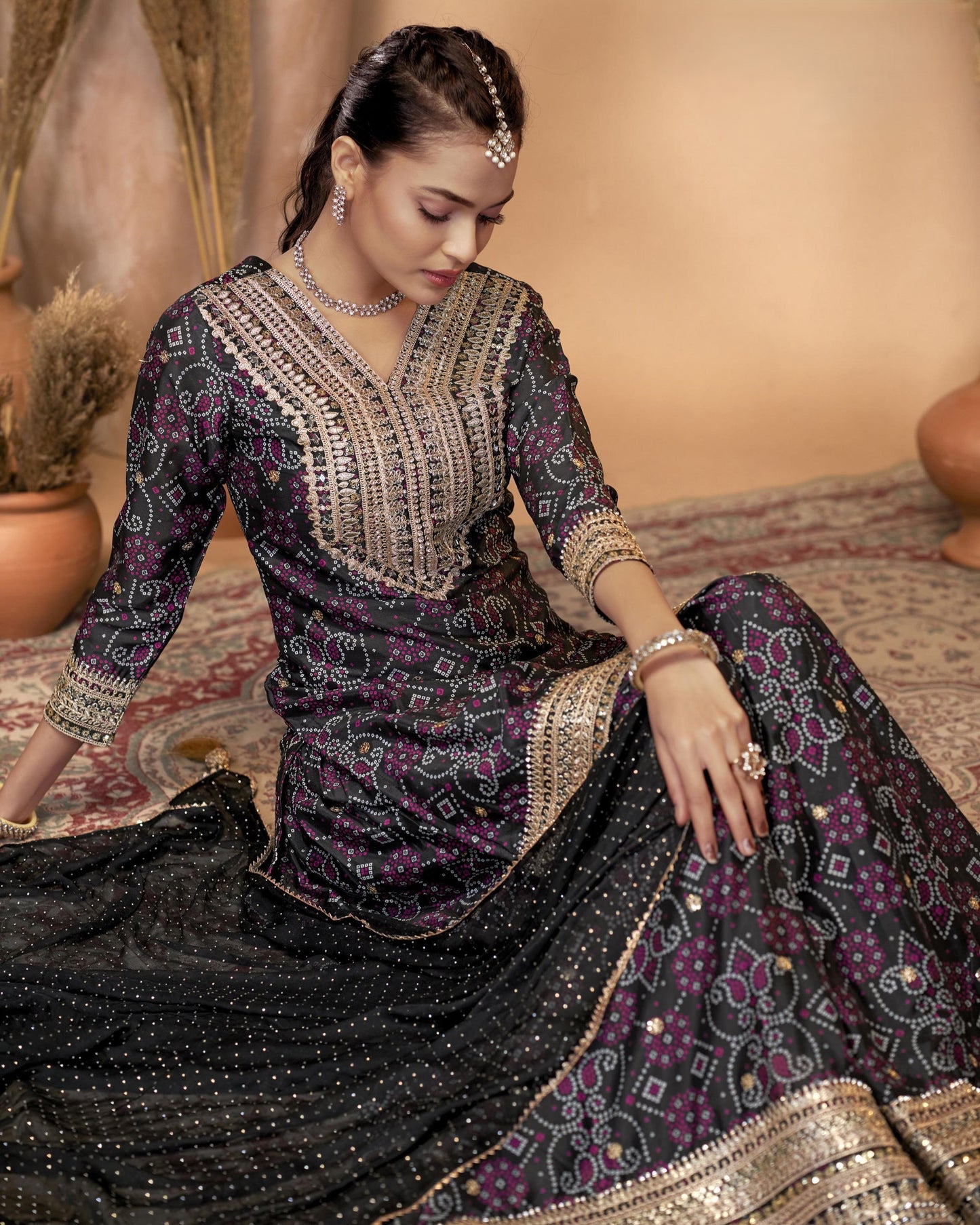 Woman in an embroidered traditional outfit sitting on a patterned rug.