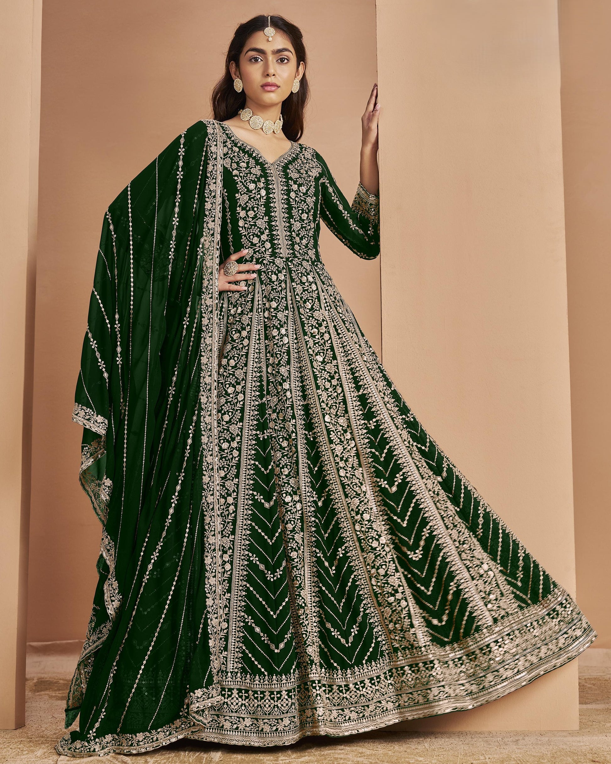 Woman wearing a green and silver embroidered traditional outfit against a beige background