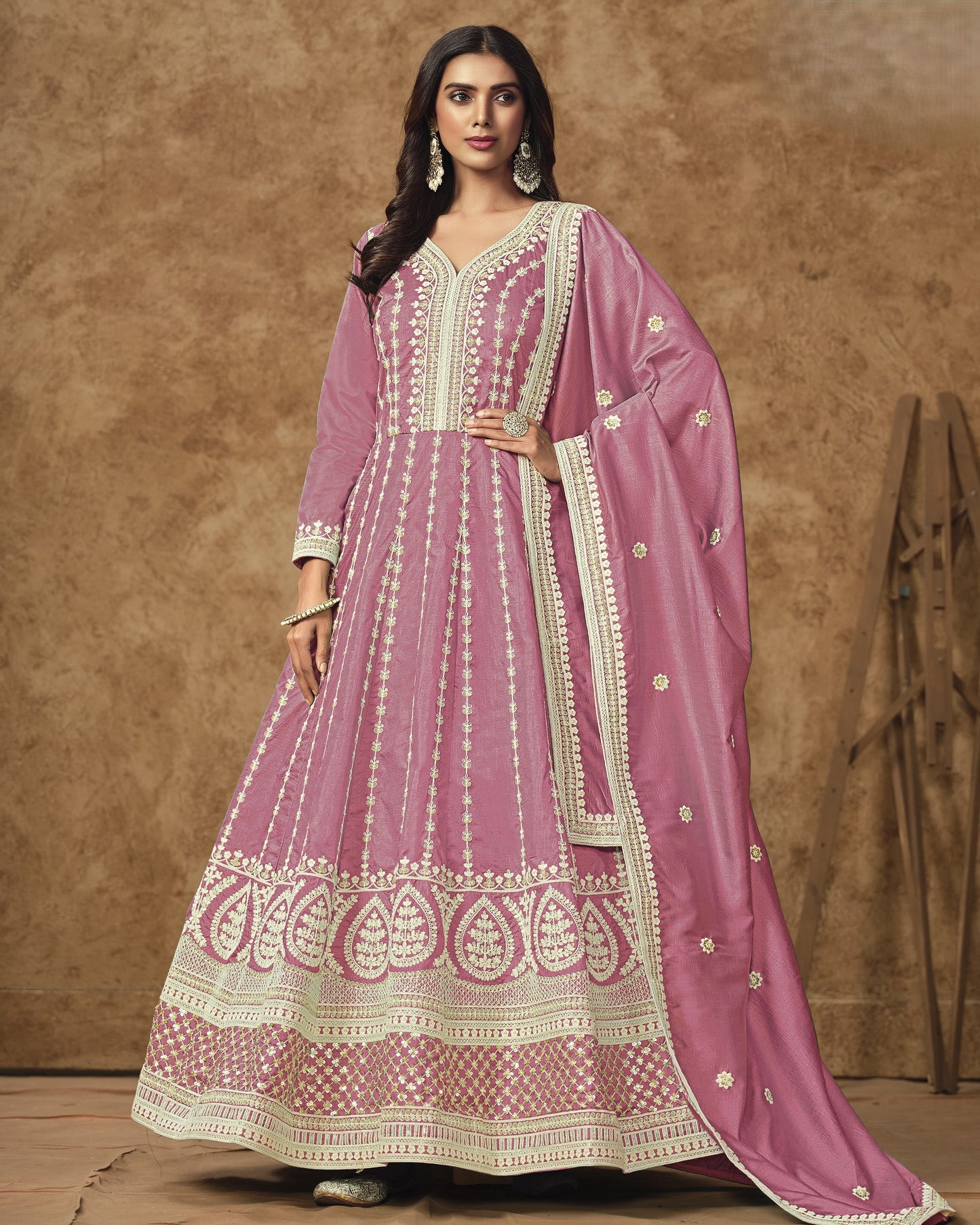 Woman wearing a pink traditional outfit with white embroidery against a brown background