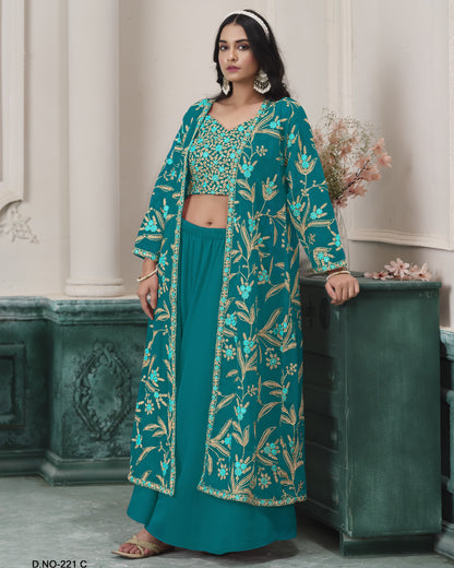 Woman wearing a teal embroidered outfit standing against a decorative wall.