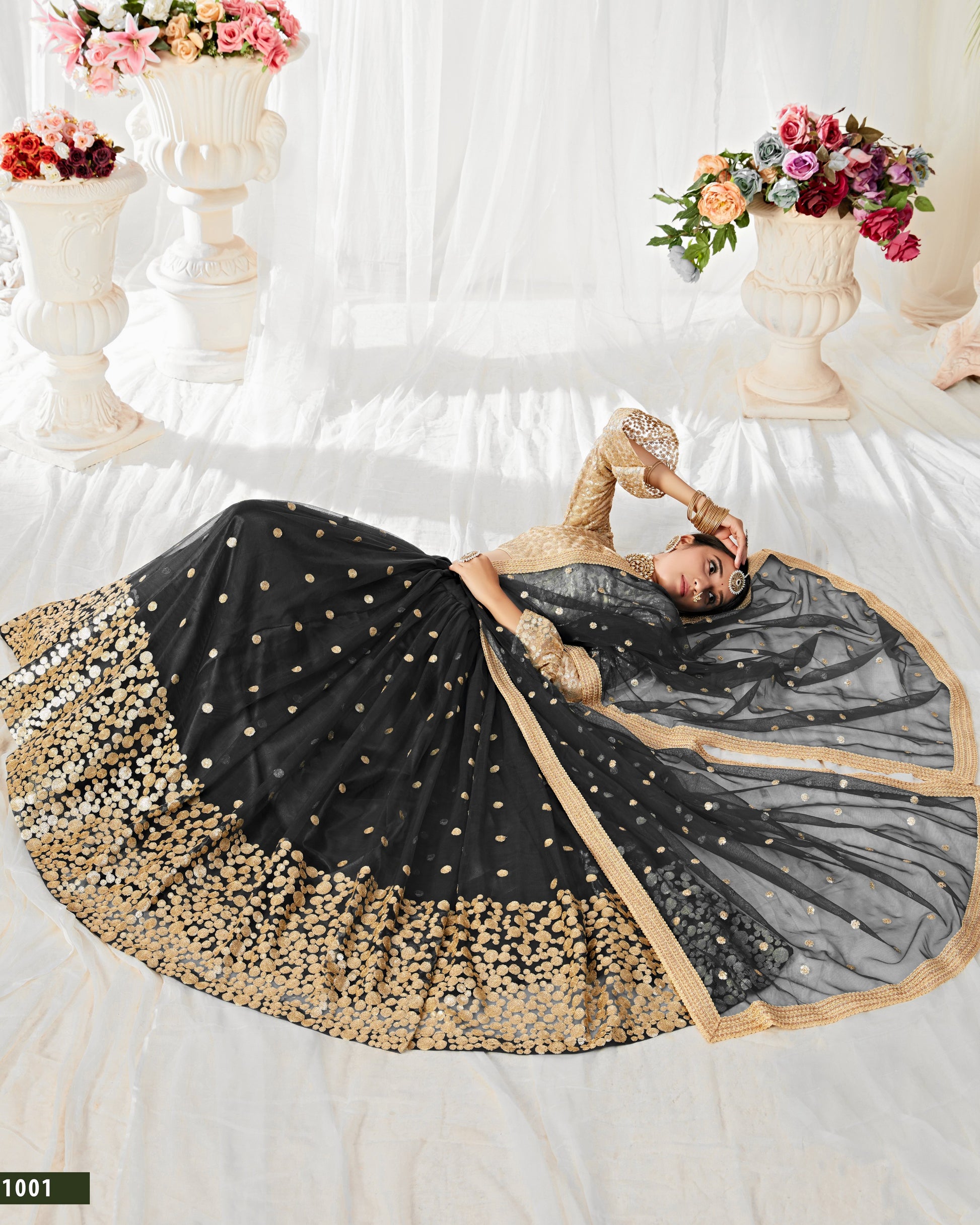 Woman in a black and gold saree lying on a white floor with floral decorations.