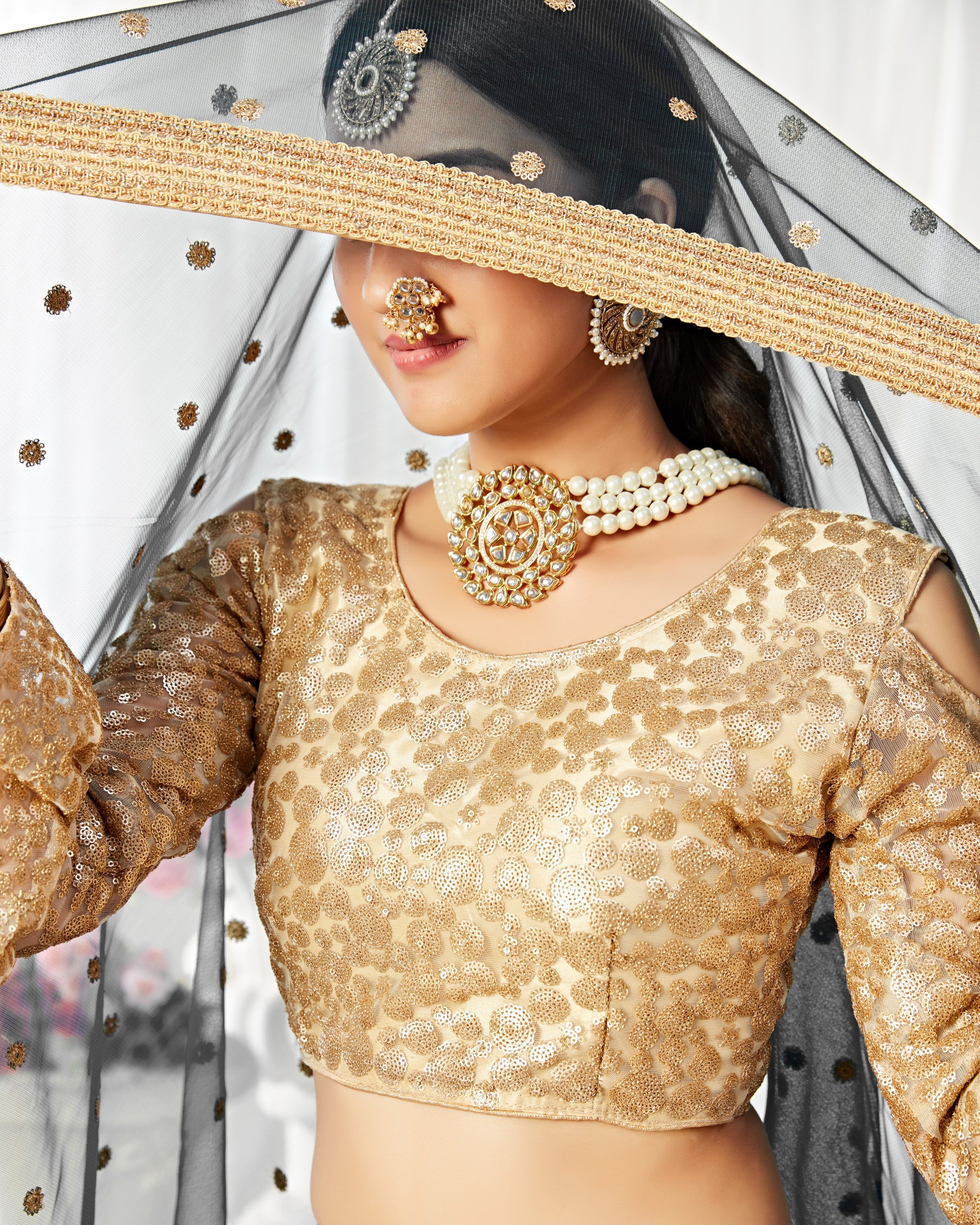 Woman wearing a gold blouse with intricate patterns and jewelry, holding a sheer fabric.