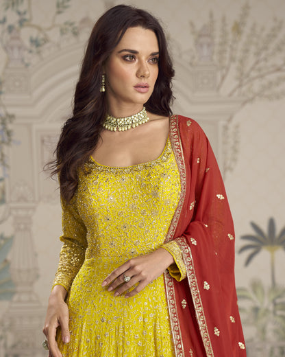 Woman in a yellow and red traditional outfit with intricate patterns against a decorative background