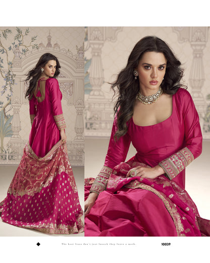 Woman in a pink traditional outfit with intricate designs, sitting against a decorative wall.