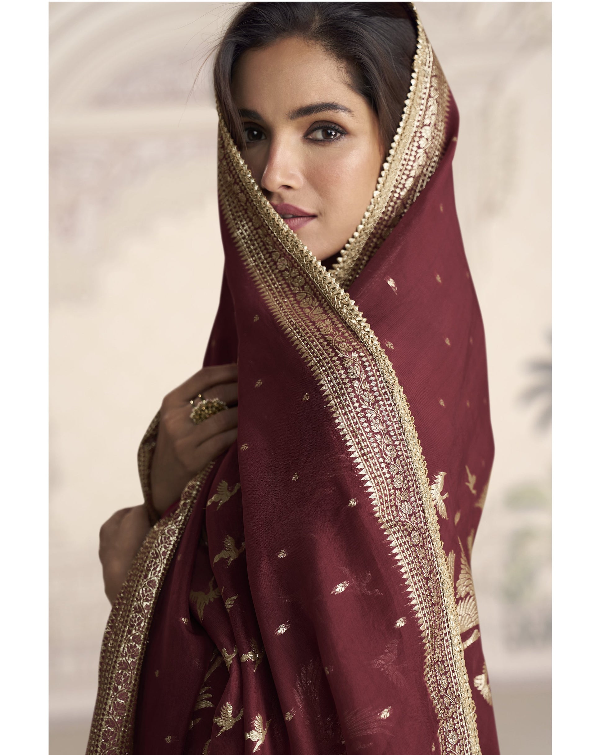 Woman wearing a maroon saree with gold embroidery against a neutral background
