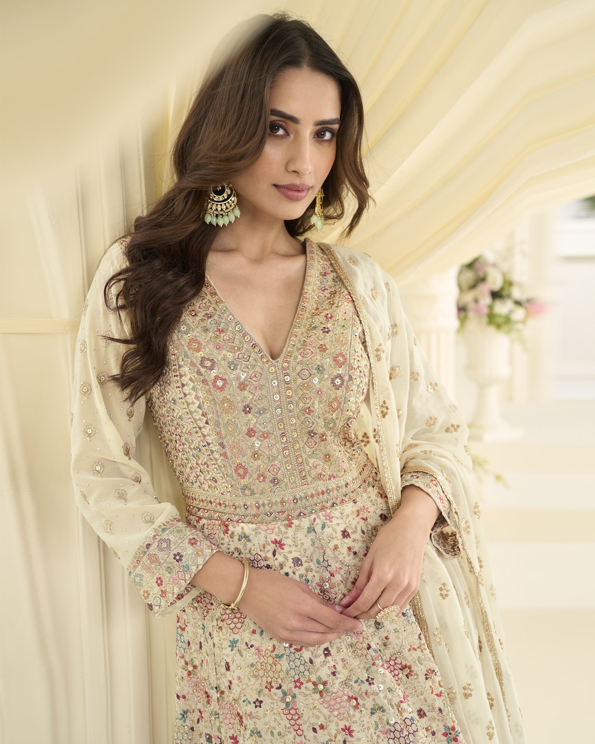 Woman wearing a floral dress with a sheer dupatta in a softly lit room.