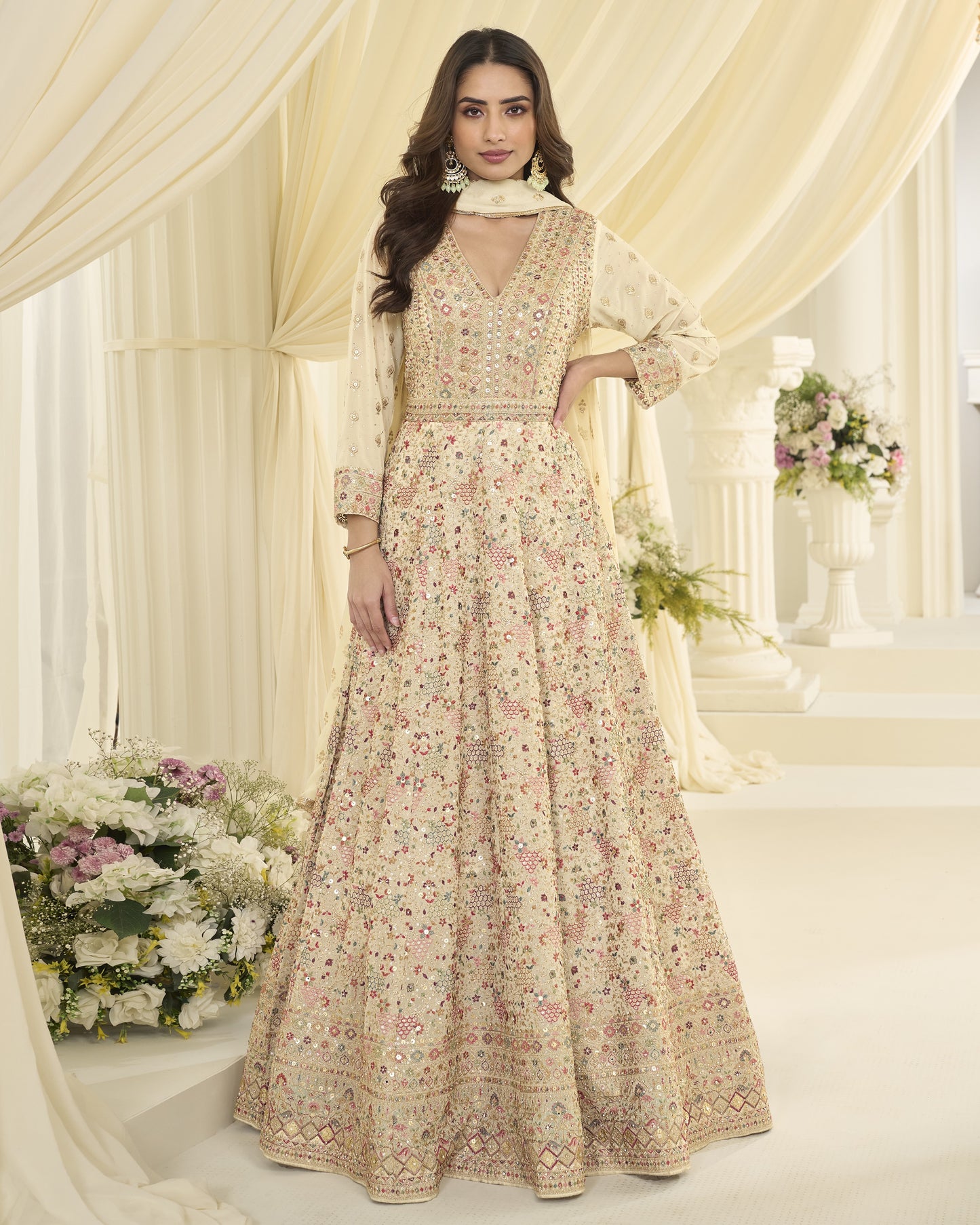 Woman in a floral dress standing in a decorated indoor setting with flowers and curtains.