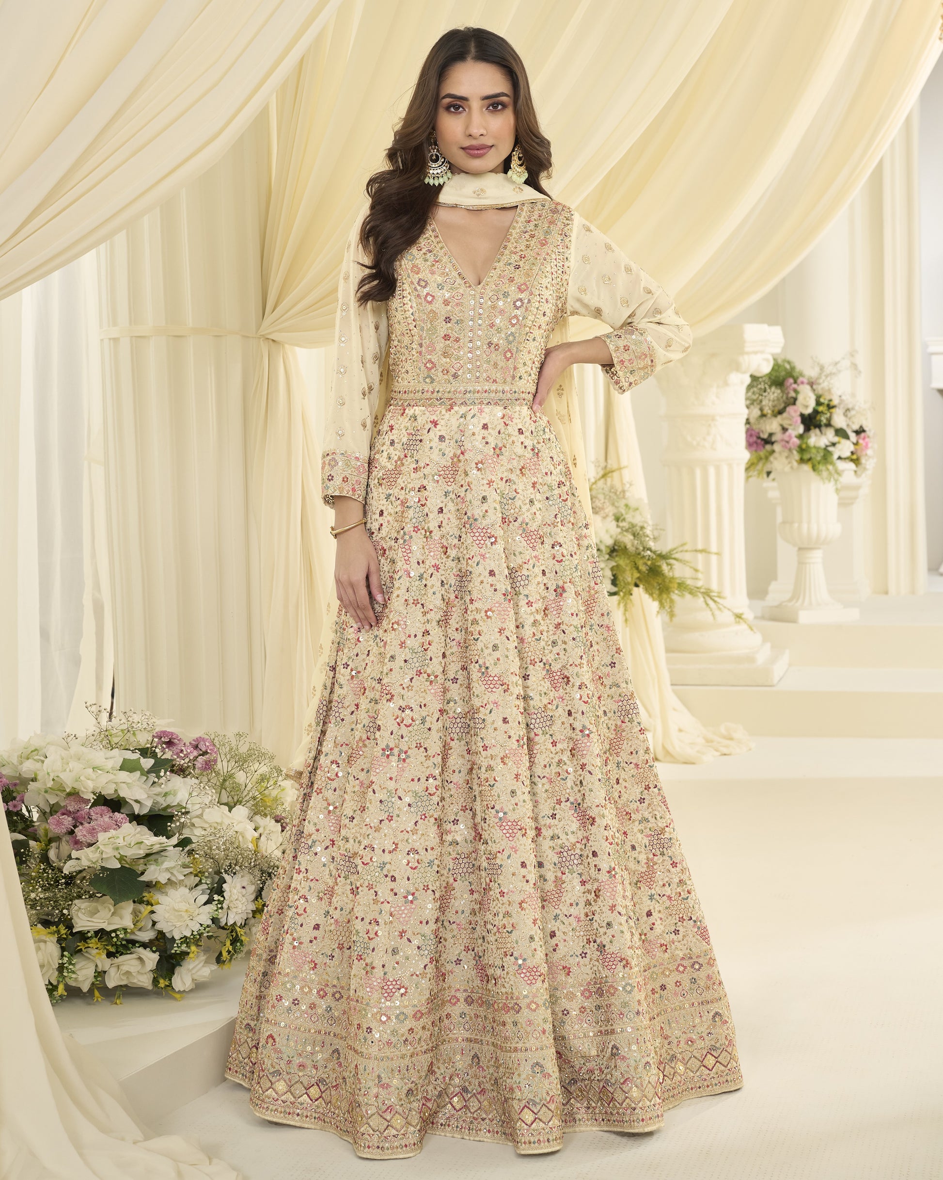 Woman in a floral dress standing in a decorated indoor setting with flowers and curtains.