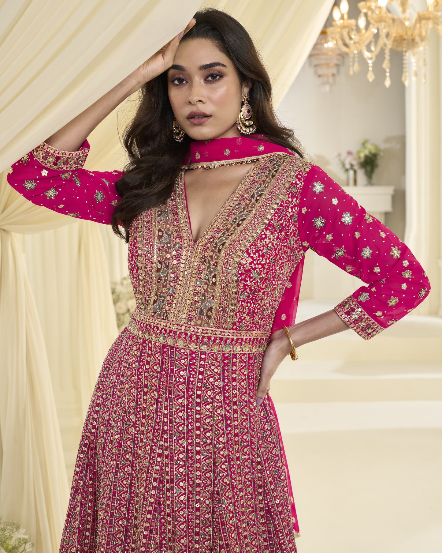 Woman wearing a pink and red embroidered traditional outfit in an elegant indoor setting.
