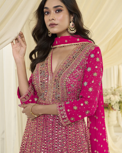 Woman wearing a pink embroidered traditional outfit with gold jewelry against a neutral background
