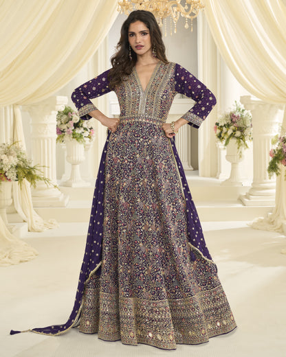 Woman in a long, patterned dress standing in an elegant indoor setting with floral arrangements and chandeliers.