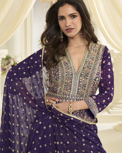 Woman wearing a traditional embroidered outfit with a purple dupatta in an elegant indoor setting.