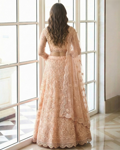 Woman in a peach lace dress standing in front of large windows.