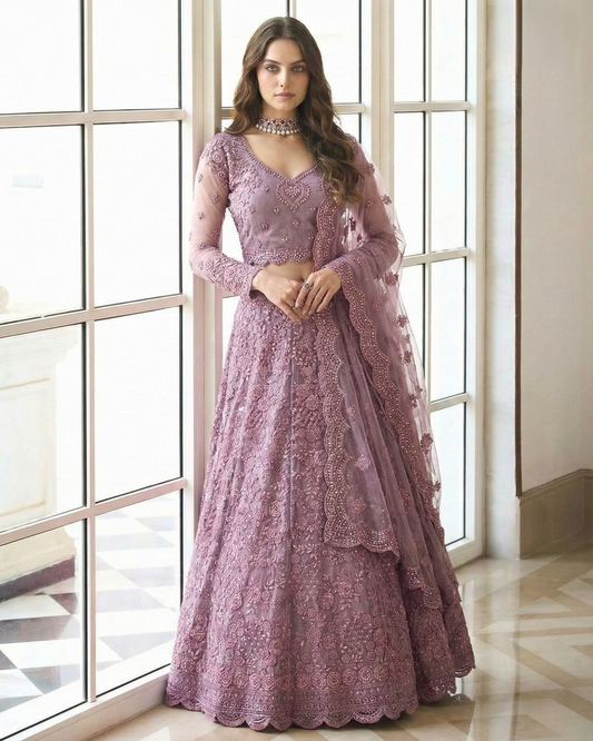 Woman wearing a pink lace dress standing in a room with large windows.