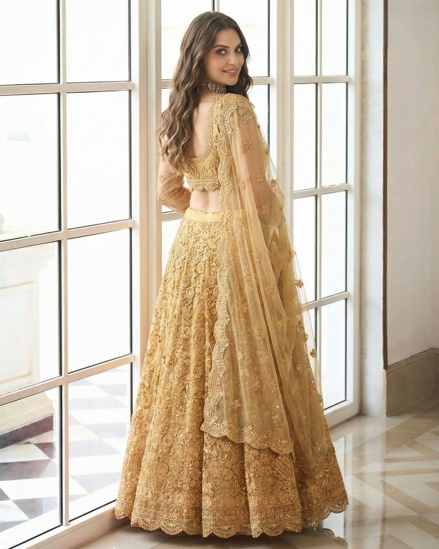 Woman in a gold embroidered traditional outfit standing in front of large windows.