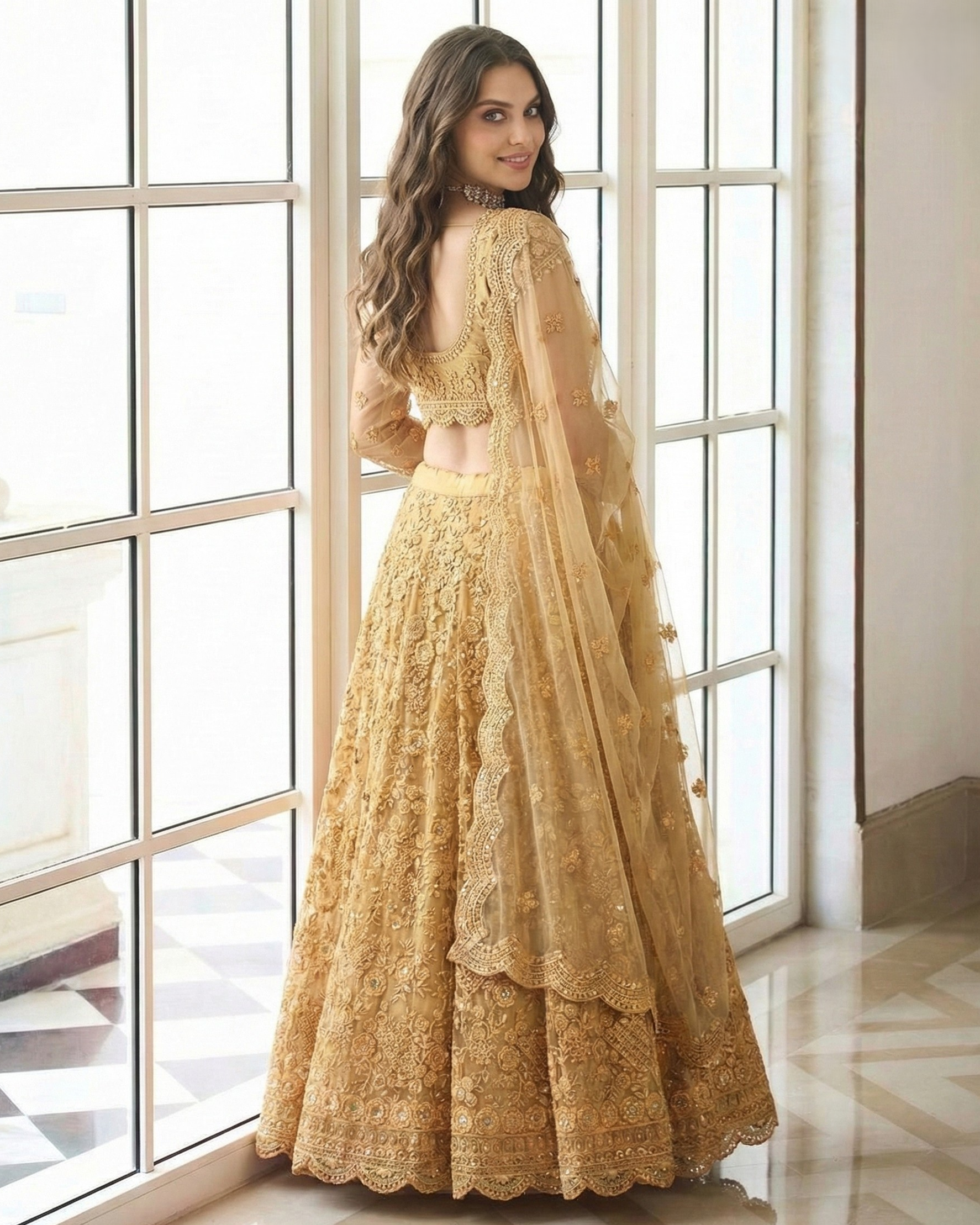 Woman in a gold embroidered traditional outfit standing in front of large windows.