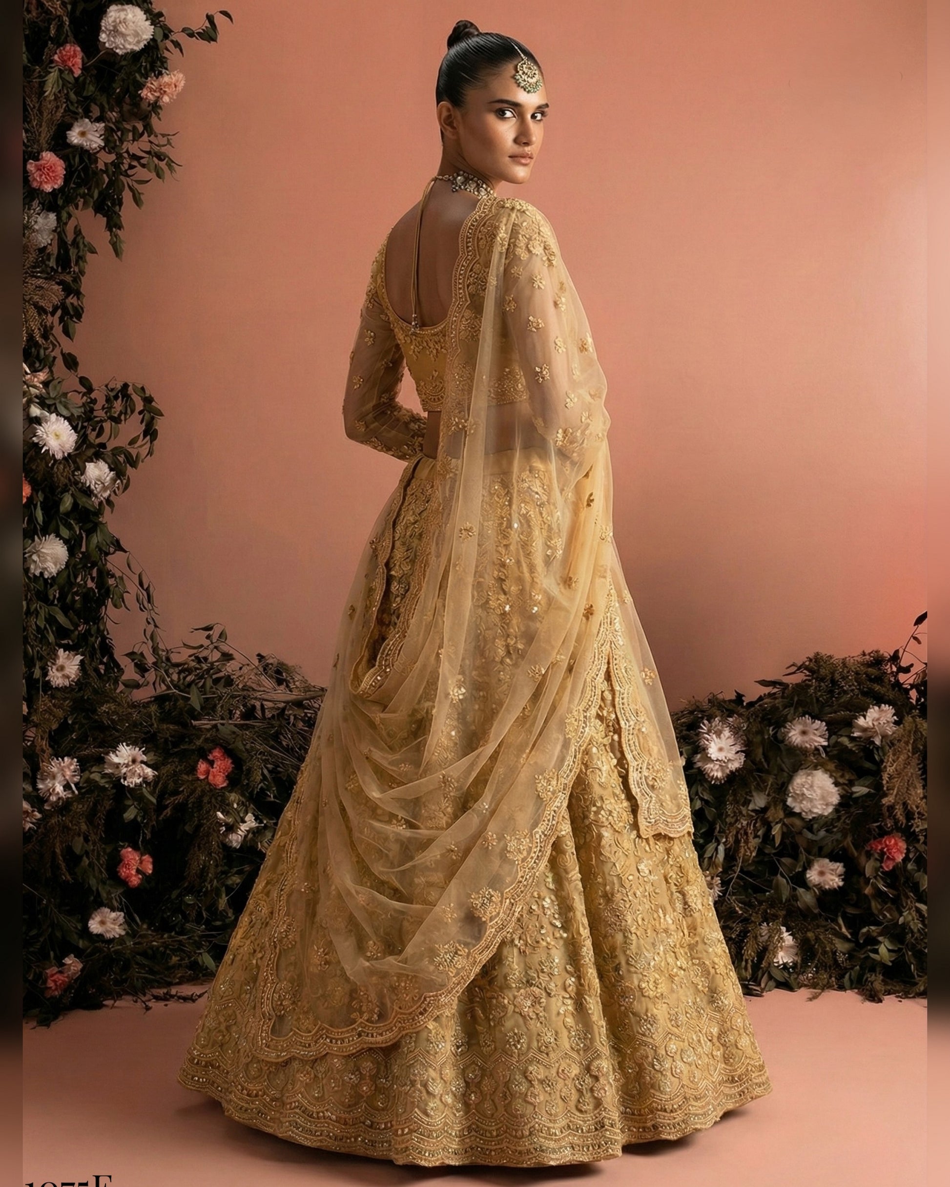 Woman in a gold embroidered traditional outfit standing against a floral decorated backdrop.