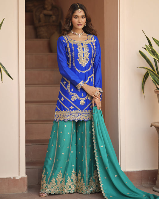 Woman wearing a blue and green embroidered traditional outfit indoors.