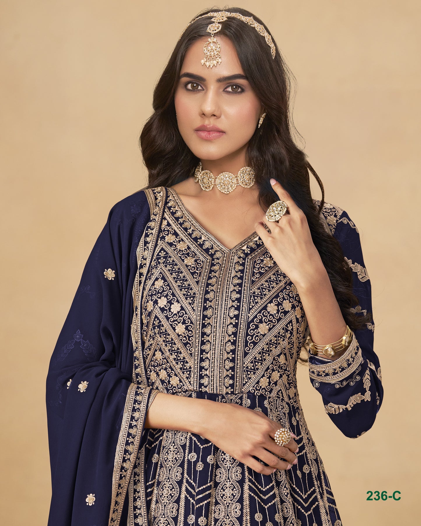 Woman wearing a navy blue and gold embroidered traditional outfit with jewelry on a beige background
