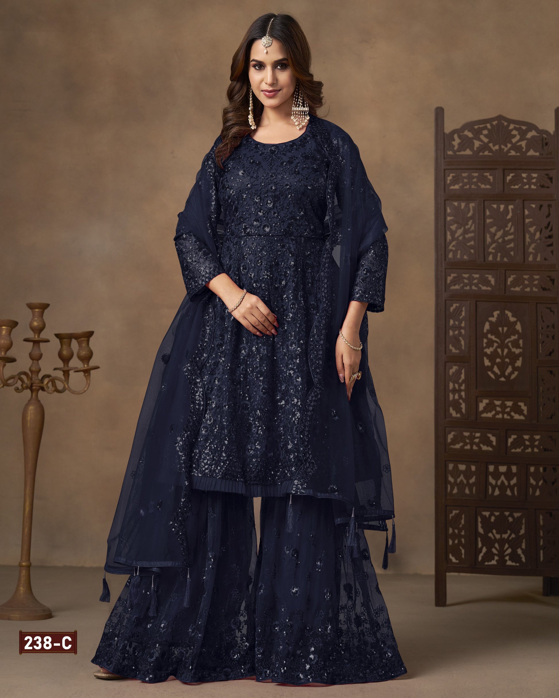 Woman wearing a navy blue traditional outfit with intricate patterns against a beige background.