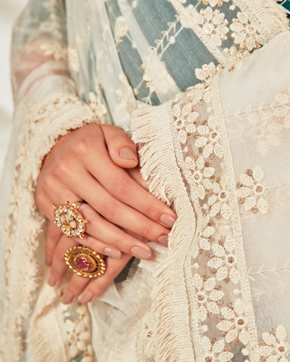 Close-up of a hand wearing gold rings with intricate designs on a textured fabric background.