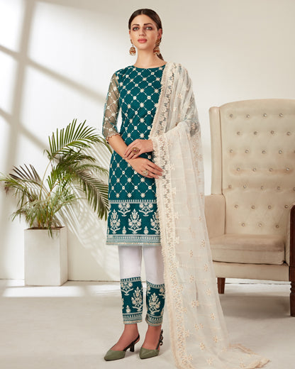 Woman wearing a teal and white traditional outfit with a beige chair and plant in the background