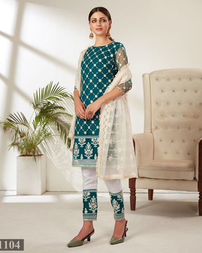 Woman wearing a teal and white traditional outfit in a bright room with a plant and chair.