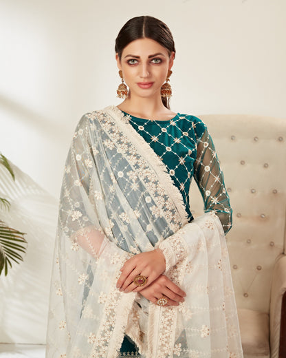 Woman wearing a traditional outfit with a green top and light-colored dupatta in an indoor setting.