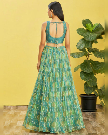 Woman wearing a green patterned outfit standing against a yellow wall with a plant.