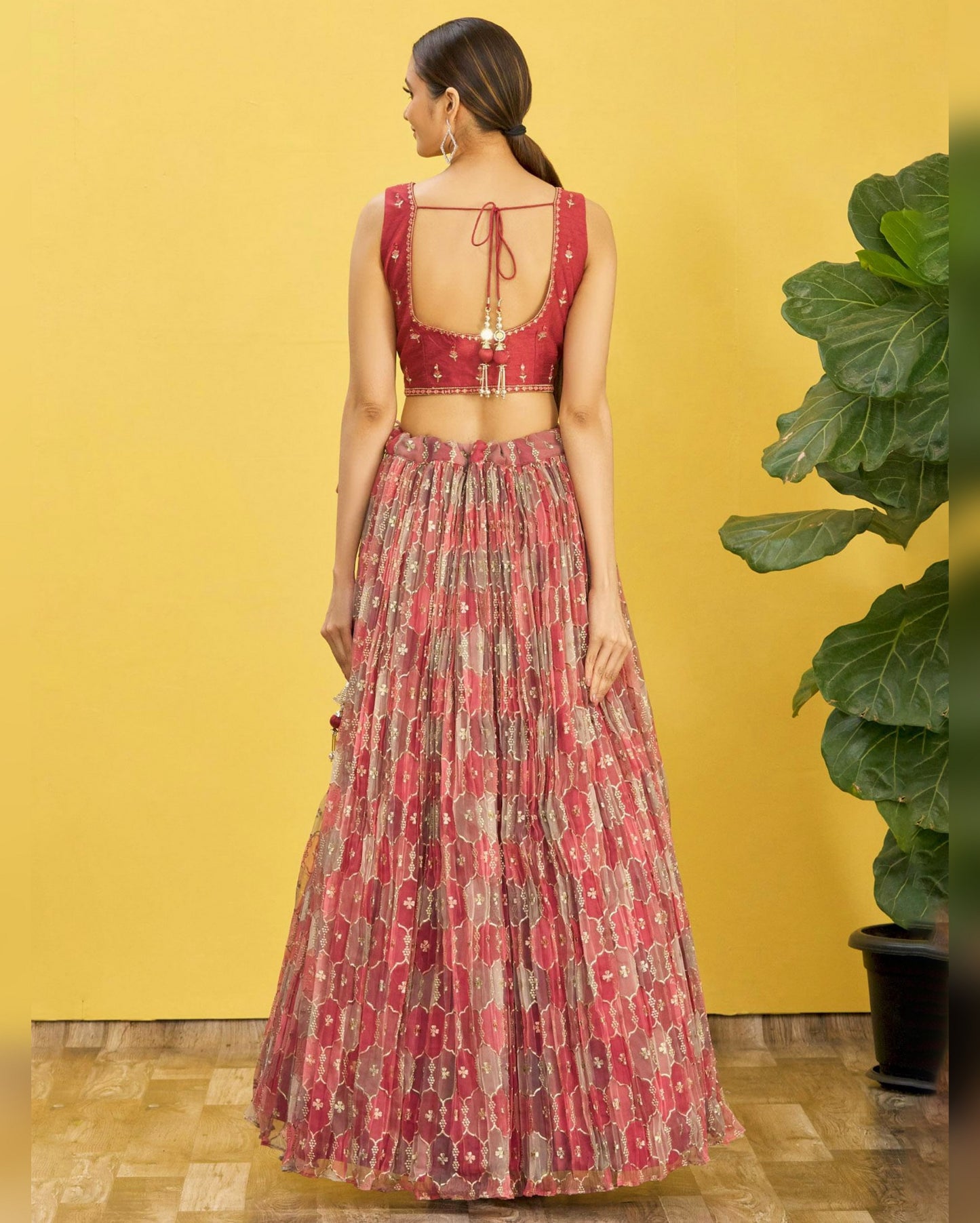 Woman wearing a red and patterned outfit against a yellow wall with a plant.