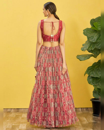 Woman wearing a red and patterned outfit against a yellow wall with a plant.