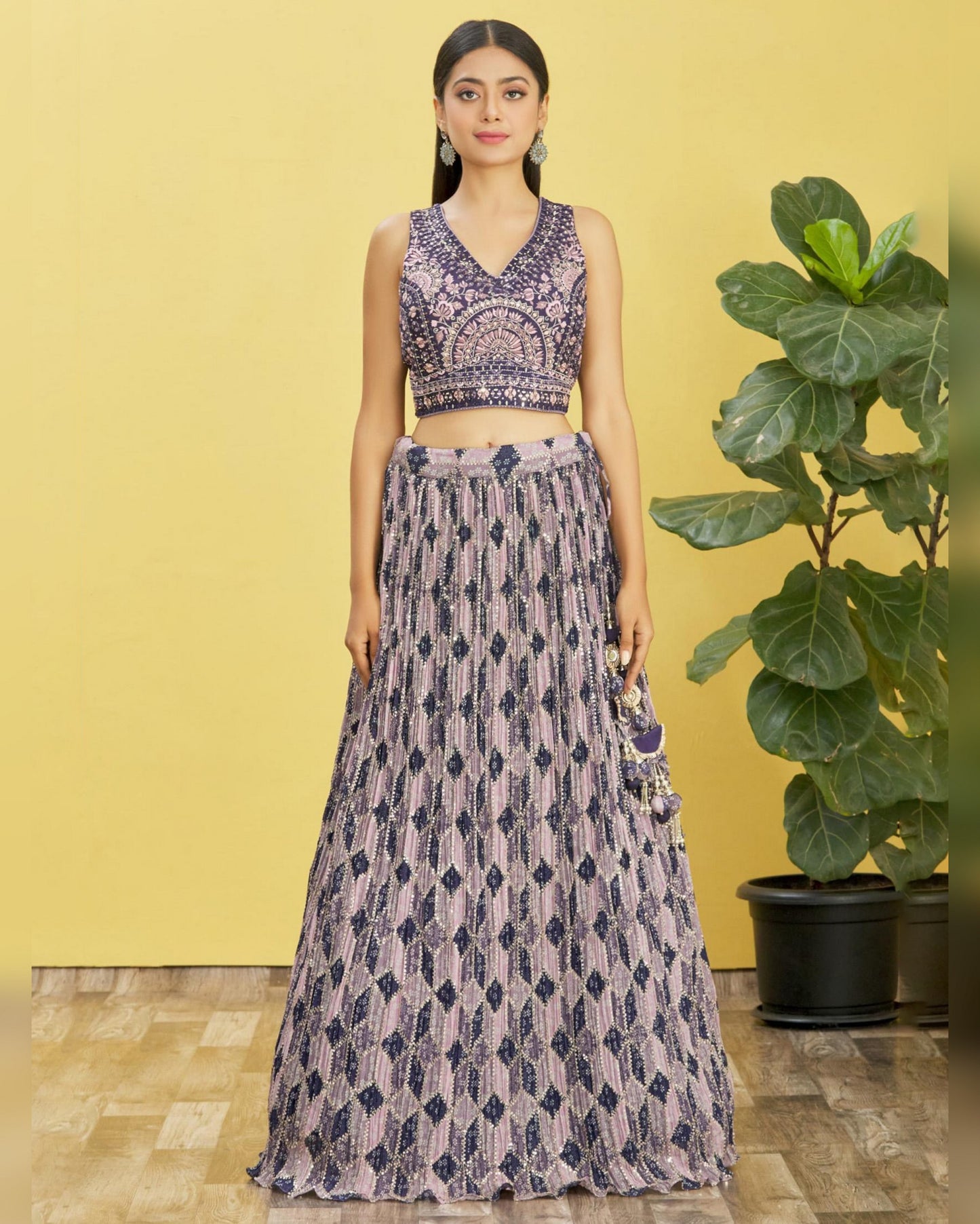 Woman wearing a patterned outfit standing against a yellow wall with a plant in the background