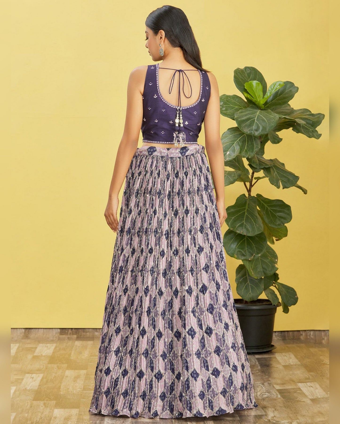 Woman wearing a patterned outfit standing against a yellow wall with a plant.