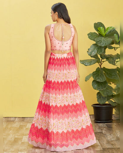 Woman wearing a pink and white patterned dress standing against a yellow wall with a plant.